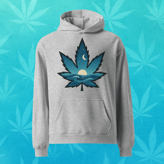 Oversized cobalt-grey hoodie featuring a stylized cannabis leaf filled with ocean waves, rising sun, and crescent moon—cozy surf-inspired 420 streetwear, front view.