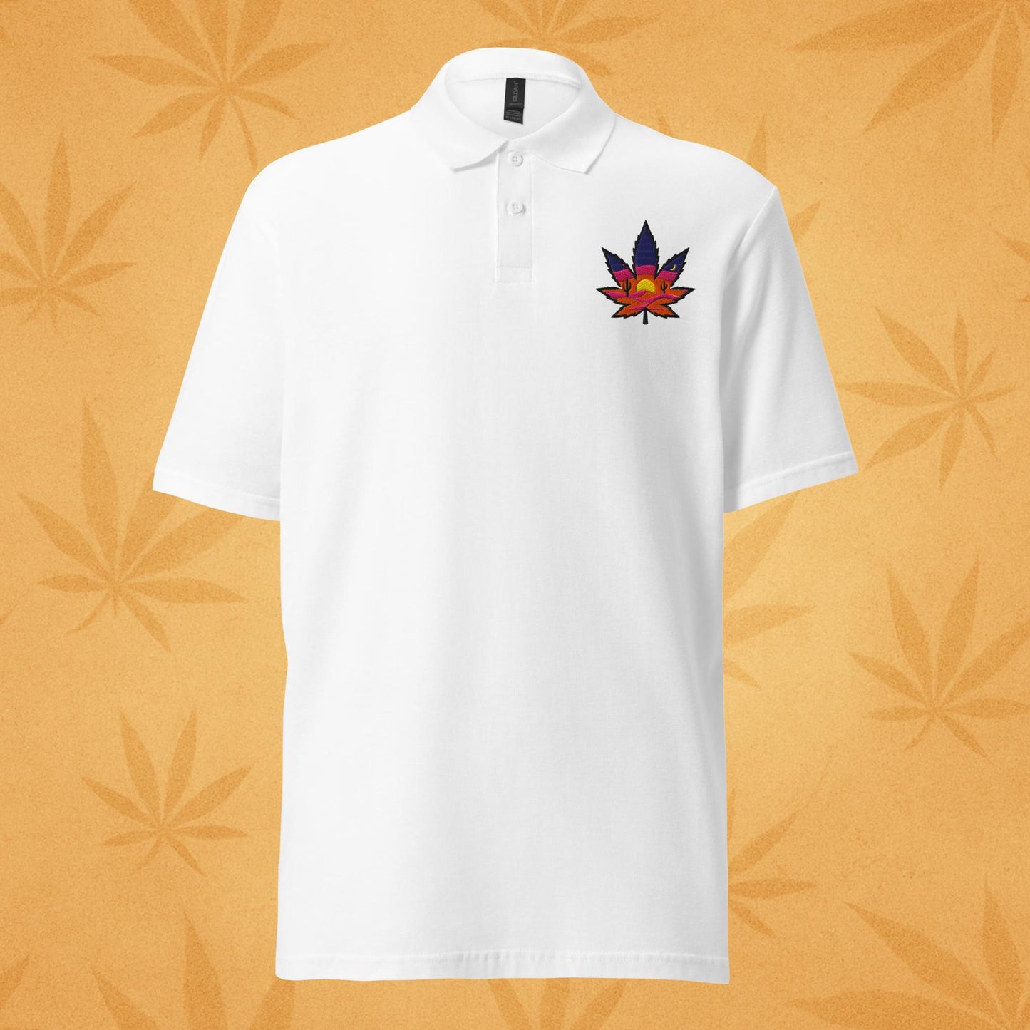 Sport-white pique polo shirt with a small embroidered sunset-colored cannabis leaf emblem on the left chest; front view against a warm desert-orange leaf backdrop.