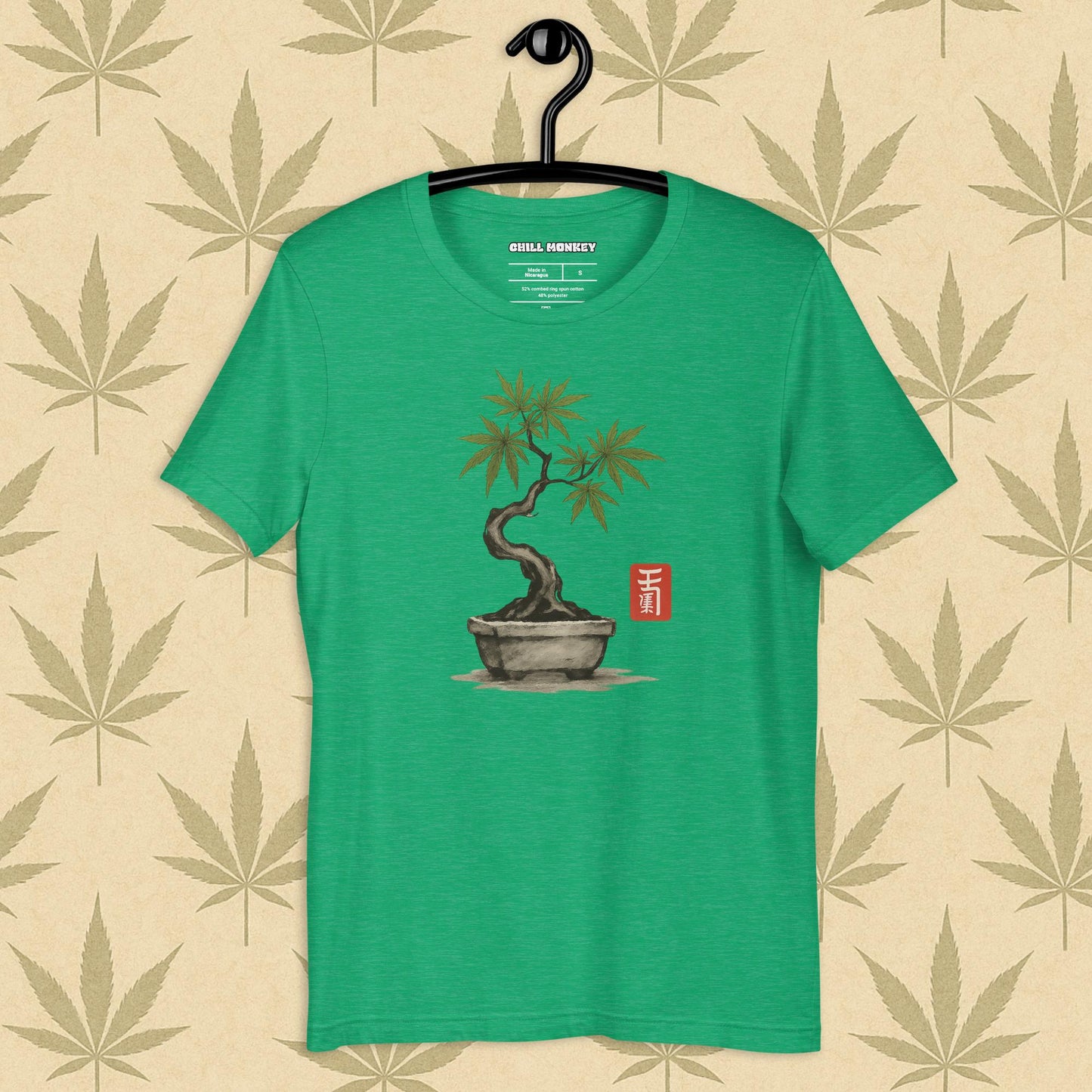 Front view of a kelly unisex Bella+Canvas tee featuring a hand-drawn cannabis-bonsai pot with Japanese-style brushwork and a small red hanko seal, shown on a neutral leaf backdrop.