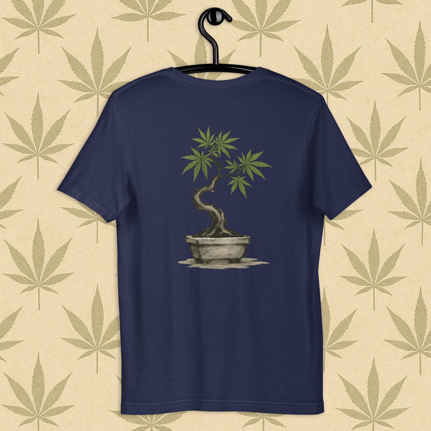 Back view of a navy unisex Bella+Canvas tee showcasing a large hand-painted cannabis-bonsai illustration in Japanese sumi-e style, centered on the shirt against a neutral leaf backdrop.
