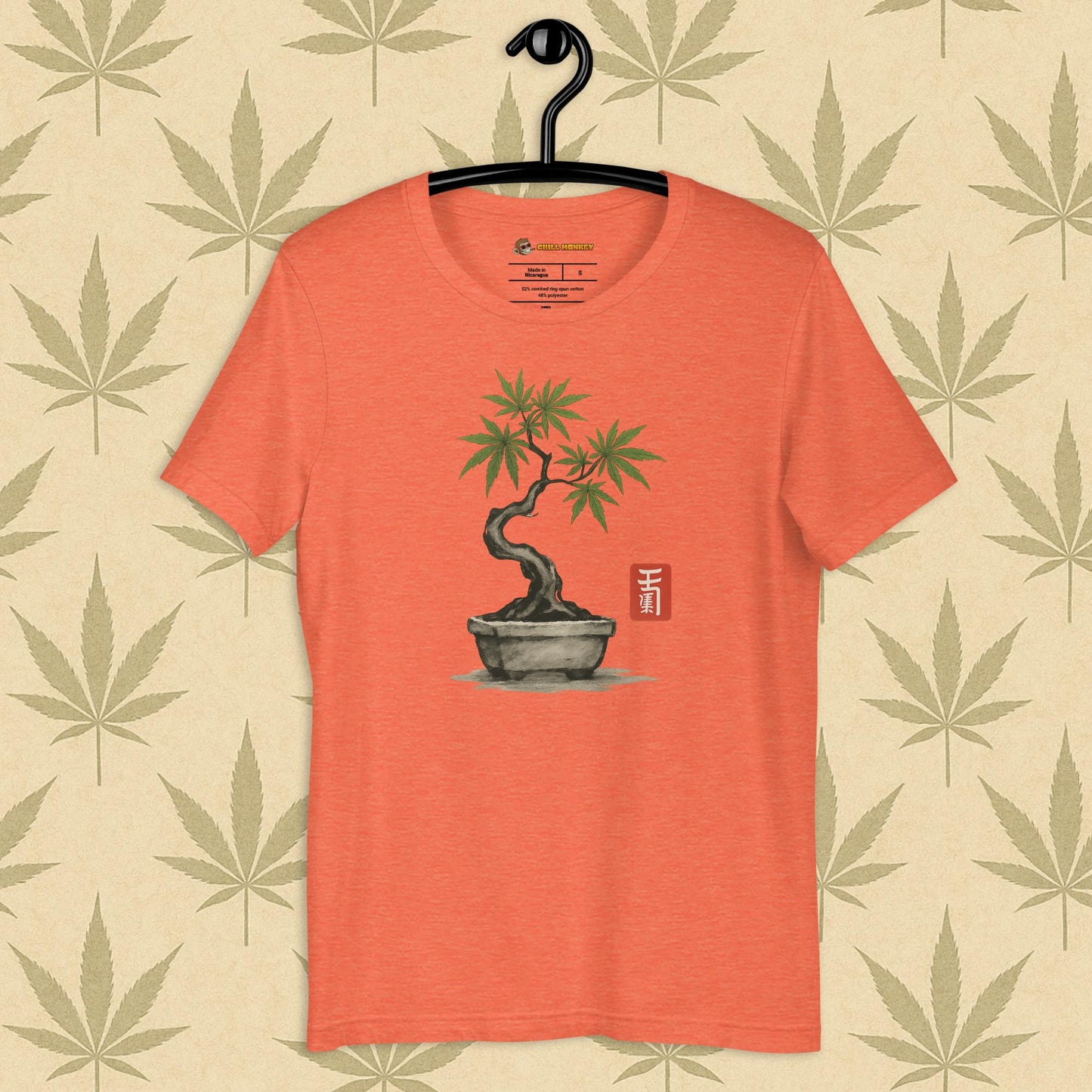 Front view of a orange unisex Bella+Canvas tee featuring a hand-drawn cannabis-bonsai pot with Japanese-style brushwork and a small red hanko seal, shown on a neutral leaf backdrop.