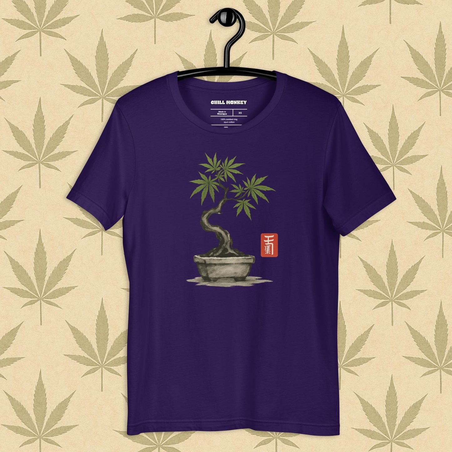 Front view of a purple unisex Bella+Canvas tee featuring a hand-drawn cannabis-bonsai pot with Japanese-style brushwork and a small red hanko seal, shown on a neutral leaf backdrop.
