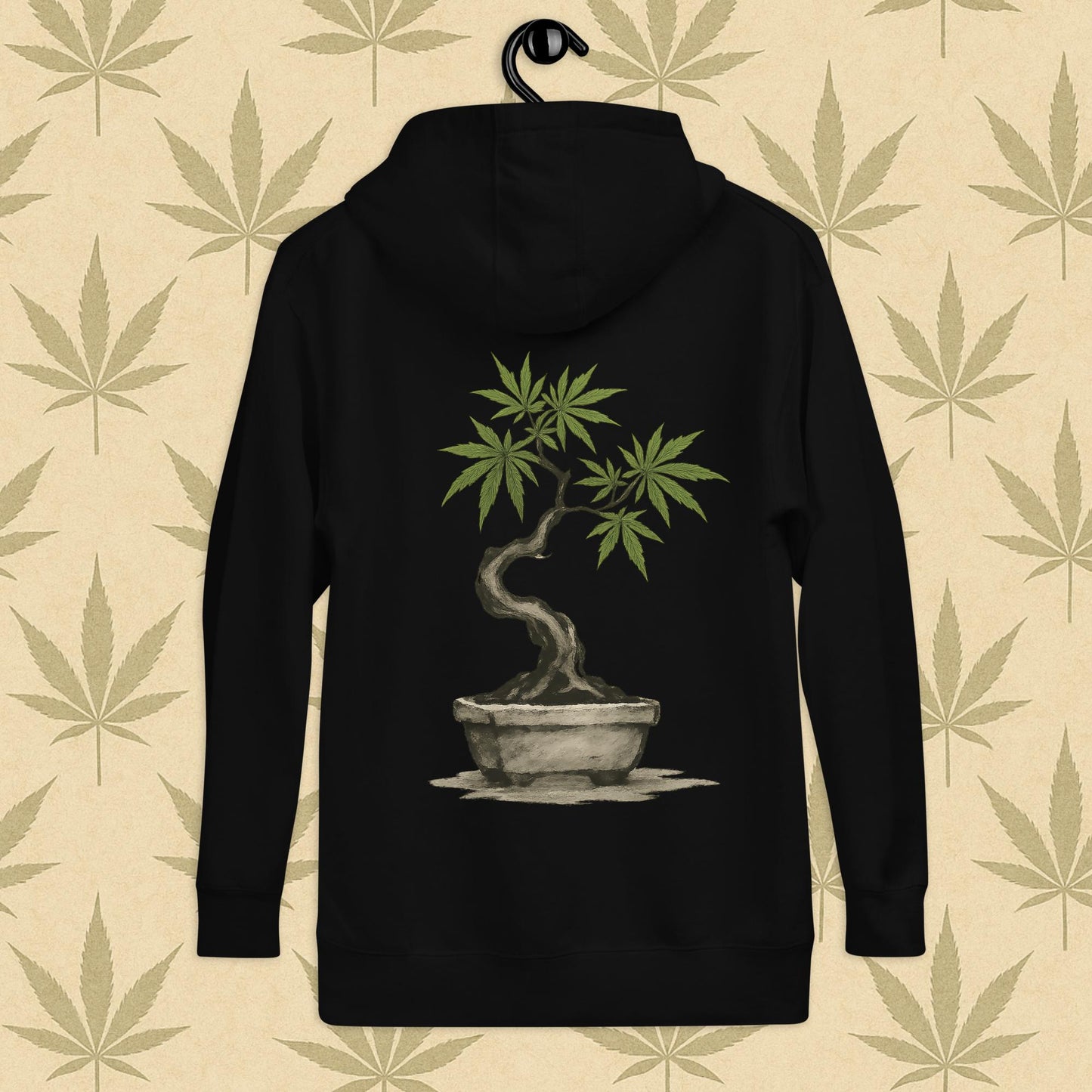 Back view of a black-colored unisex premium hoodie featuring a large Japanese sumi-e style cannabis-bonsai illustration centered on the garment against a neutral leaf backdrop.