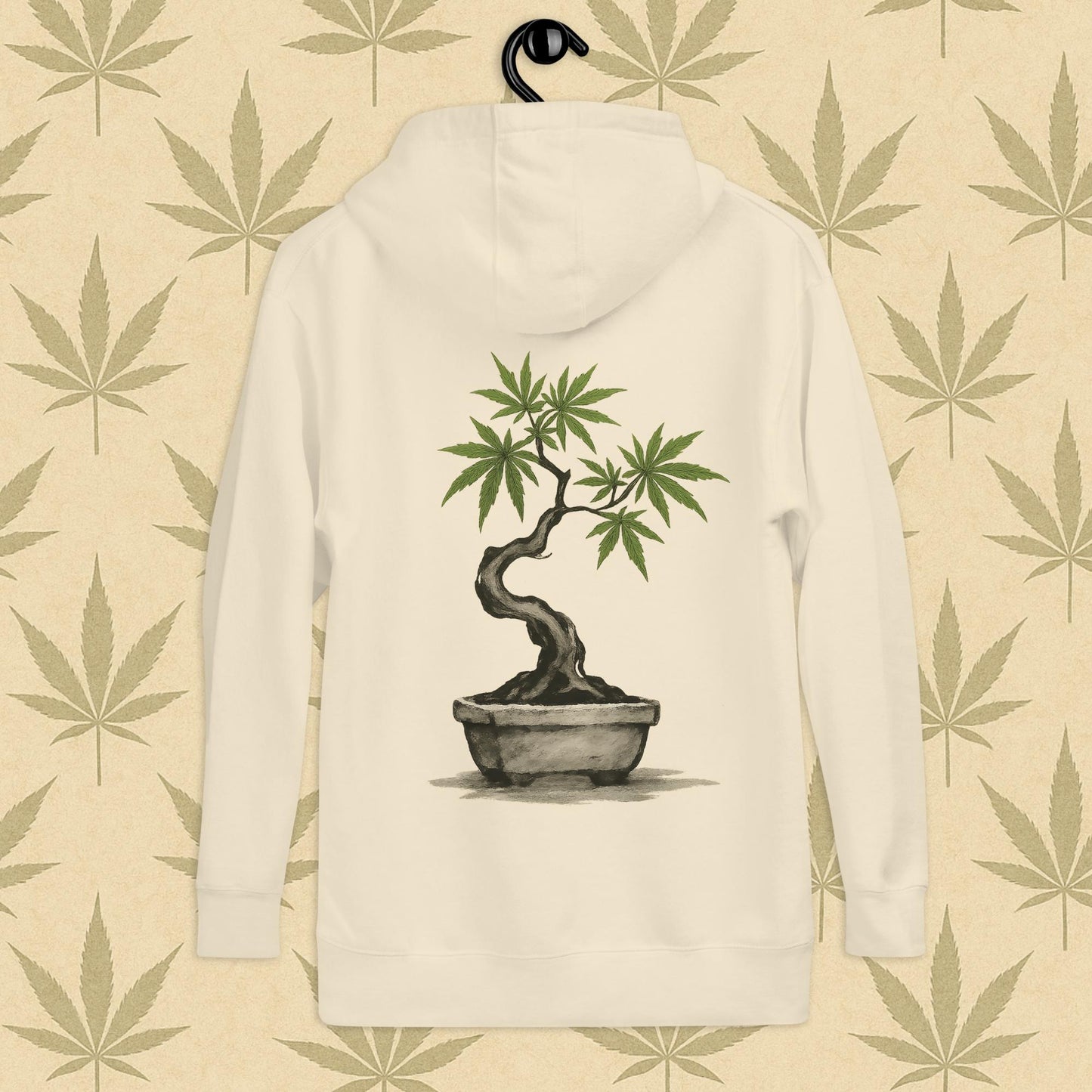 Back view of a bone-colored unisex premium hoodie featuring a large Japanese sumi-e style cannabis-bonsai illustration centered on the garment against a neutral leaf backdrop.