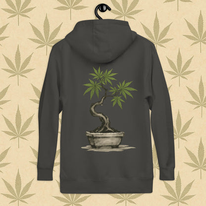 Back view of a grey-colored unisex premium hoodie featuring a large Japanese sumi-e style cannabis-bonsai illustration centered on the garment against a neutral leaf backdrop.