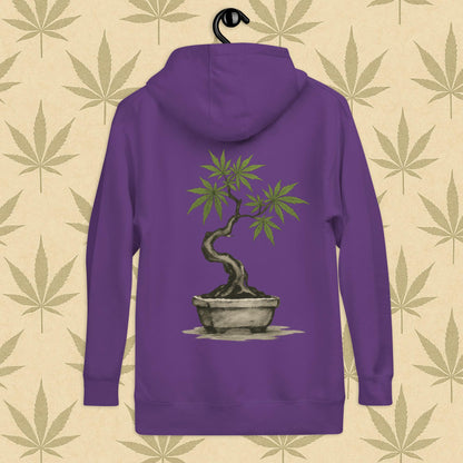 Back view of a purple-colored unisex premium hoodie featuring a large Japanese sumi-e style cannabis-bonsai illustration centered on the garment against a neutral leaf backdrop.