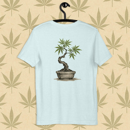 Back view of a blue unisex Bella+Canvas tee showcasing a large hand-painted cannabis-bonsai illustration in Japanese sumi-e style, centered on the shirt against a neutral leaf backdrop.