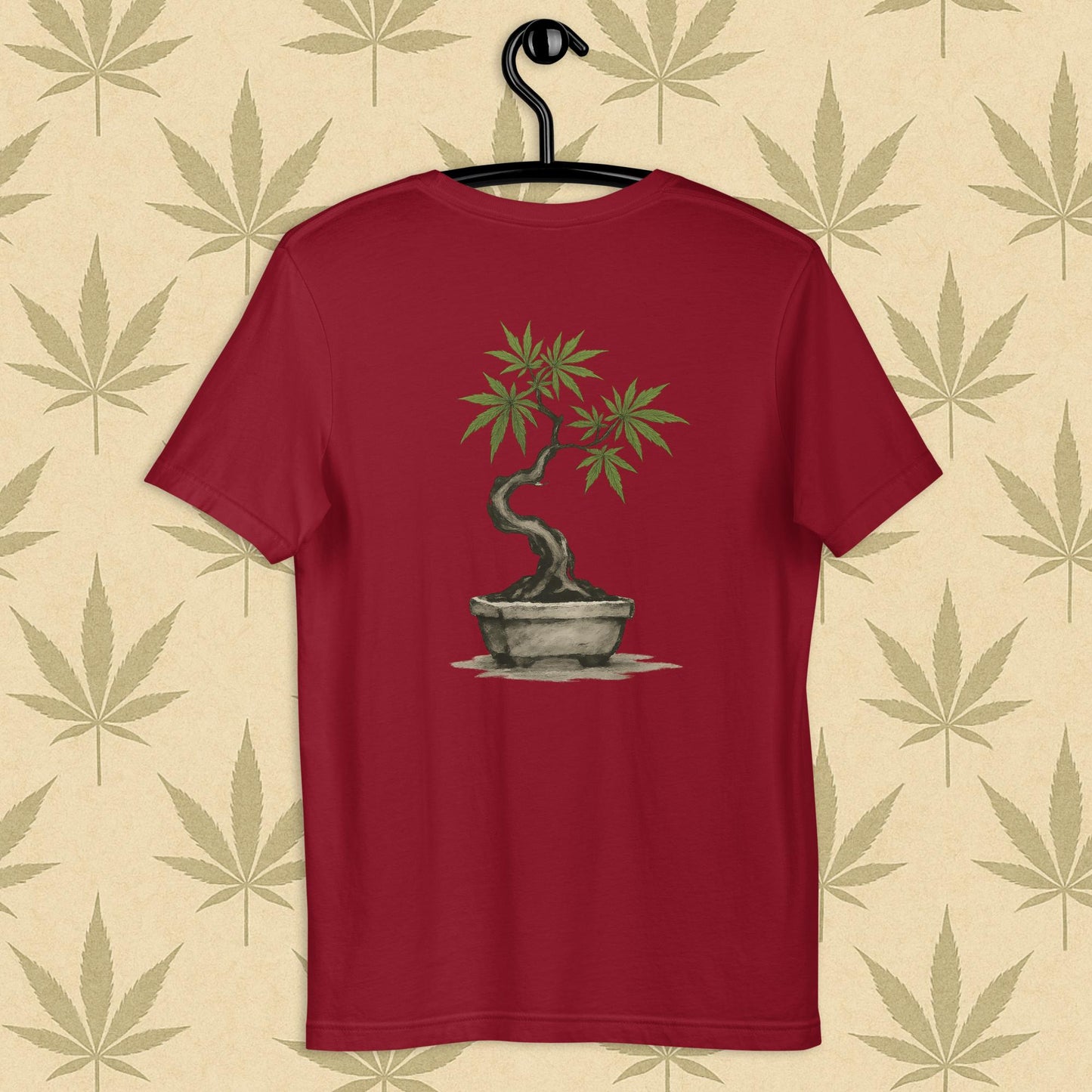 Back view of a cardinal unisex Bella+Canvas tee showcasing a large hand-painted cannabis-bonsai illustration in Japanese sumi-e style, centered on the shirt against a neutral leaf backdrop.