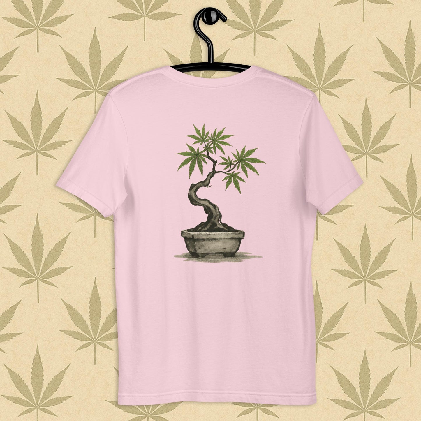 Back view of a pink unisex Bella+Canvas tee showcasing a large hand-painted cannabis-bonsai illustration in Japanese sumi-e style, centered on the shirt against a neutral leaf backdrop.