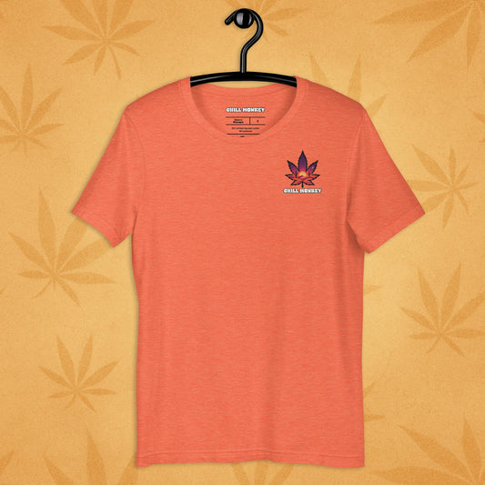 Heather-orange unisex T-shirt with a small, multicolored desert-sunset cannabis leaf emblem on the left chest; front view on a sandy, boho-leaf backdrop.